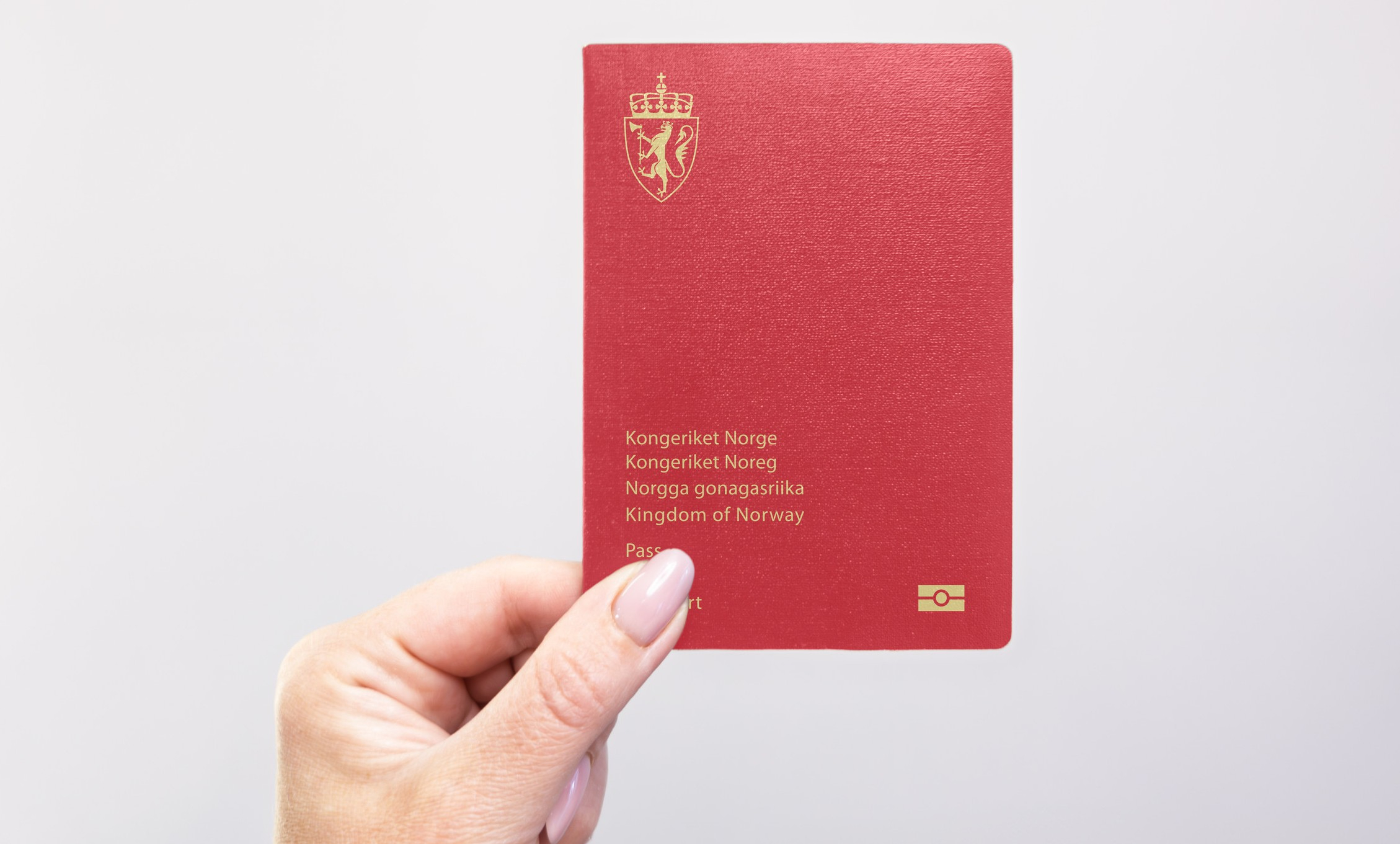 Nærbilde av et norsk pass i hånden mot en vanlig hvit bakgrunn