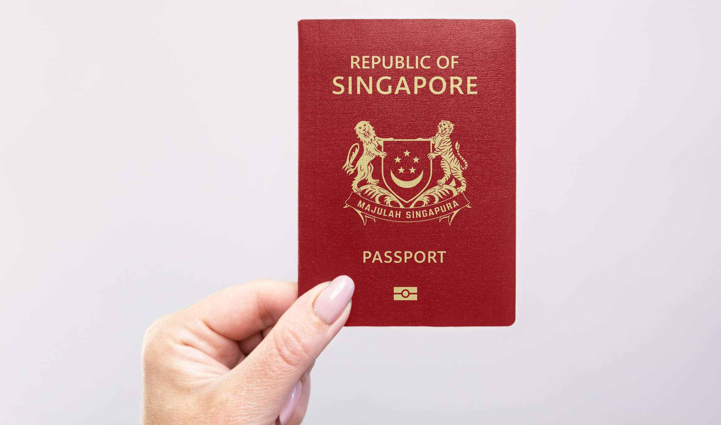 Close Up Of A Singapore Passport Held In Hand Against A Plain White Background