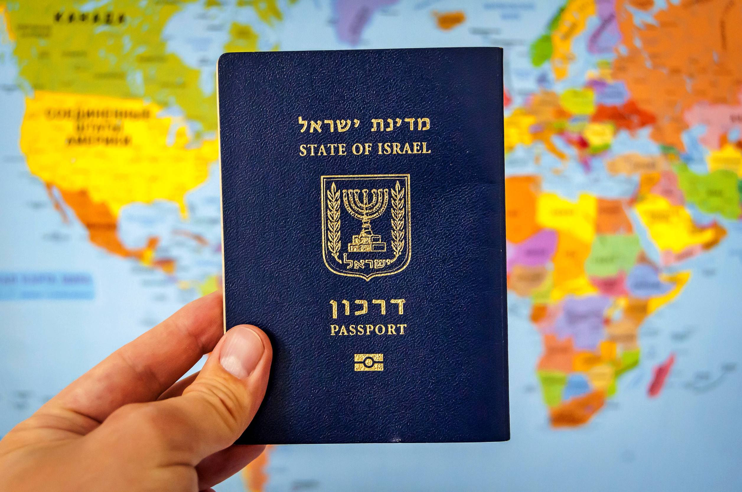 Main tenant le passeport de l'État d'Israël sur la carte du monde colorée de l'Atlas d'Israël