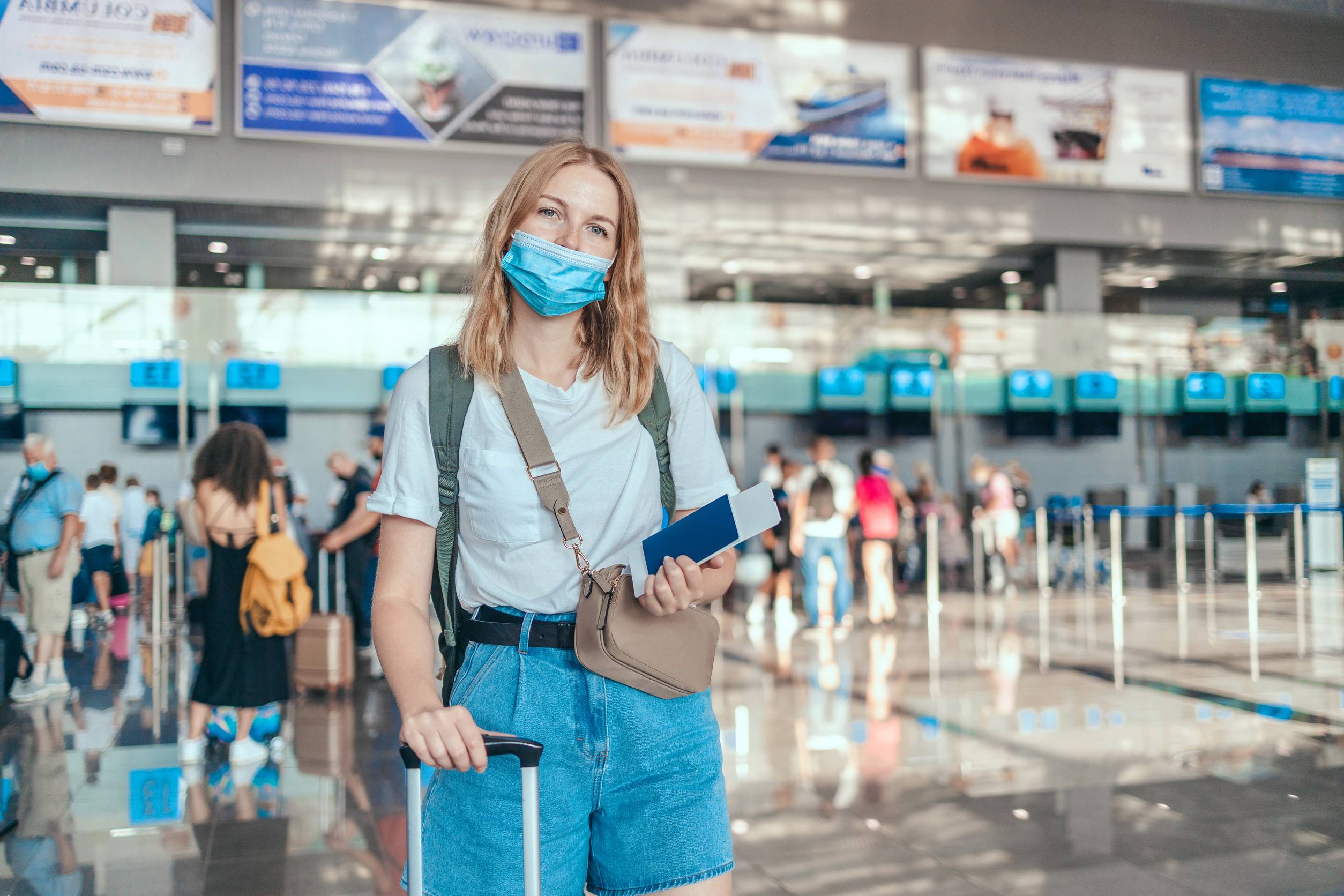 Glückliche junge Touristin mit Schutzmaske und Reisepass wartet auf den Check-in