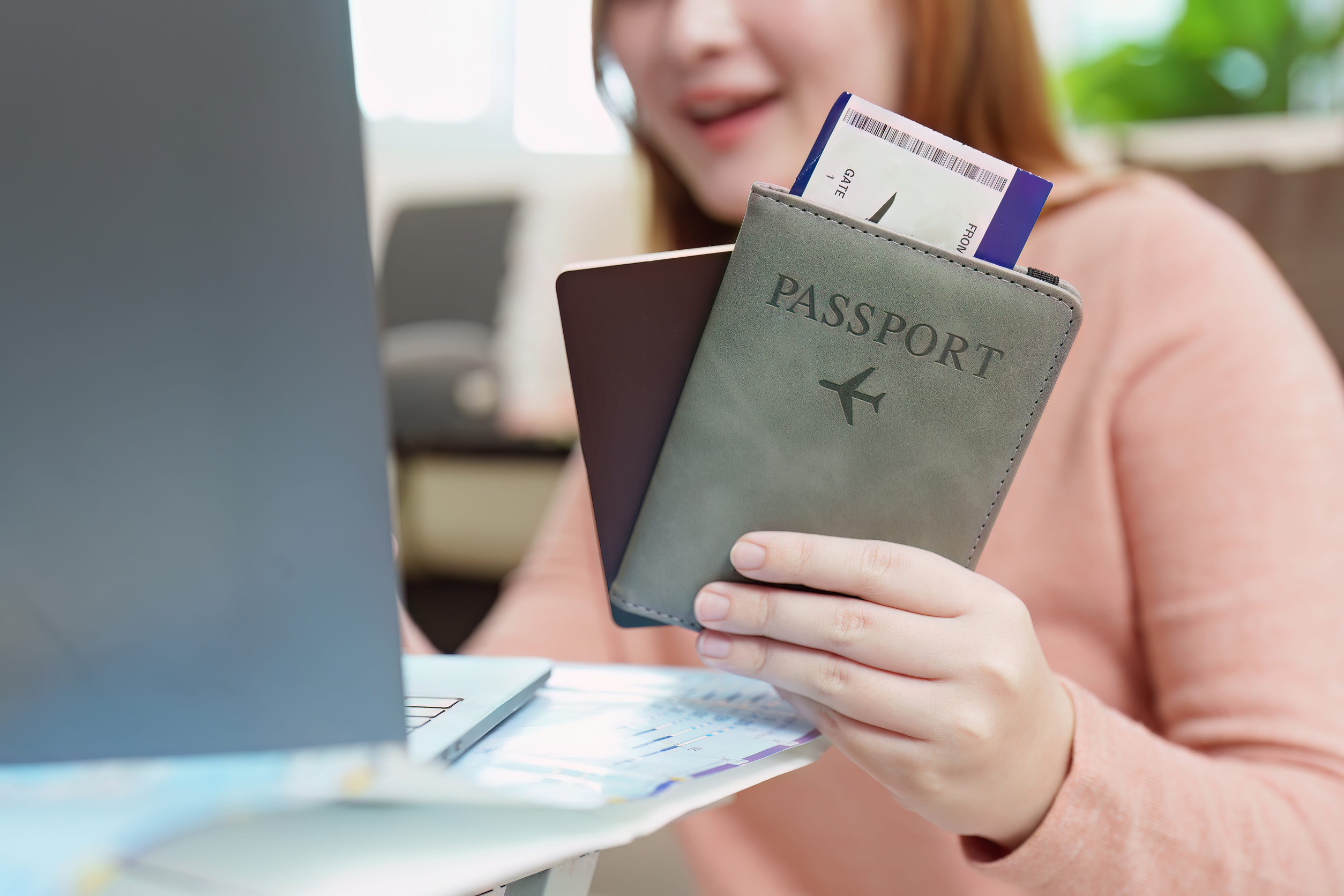 Woman Holding A Passport And Boarding Pass While Using A Laptop
