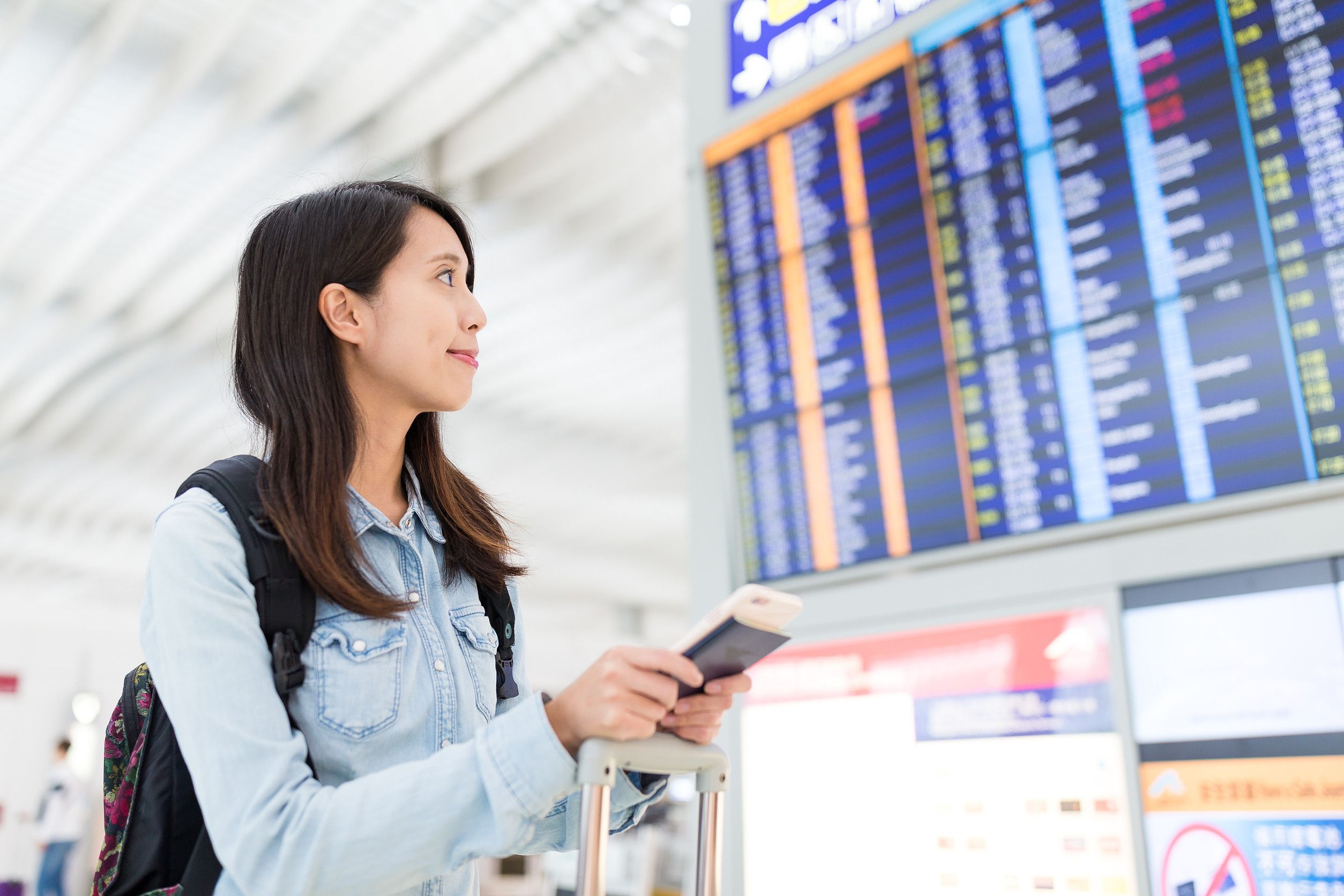 Woman Looking At Information Board In Airport With Passport